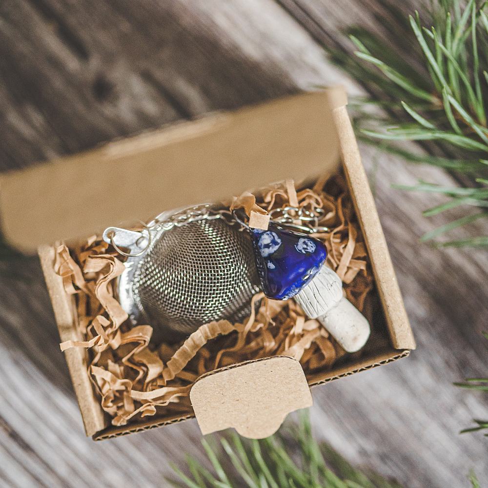 Tea infuser with ceramic blue mushroom hanging from the chain. Packed in a paper gift box.