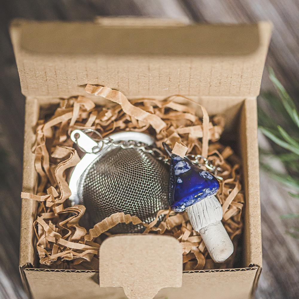 Tea infuser with ceramic blue mushroom hanging from the chain. Packed in a paper gift box.
