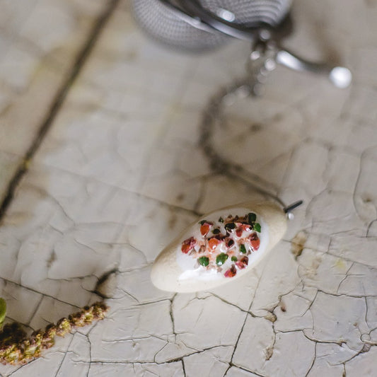 Stainless steel loose leaf tea infuser featuring a hand-made ceramic cepelinas (potato meat dumpling) charm hanging from the chain.
