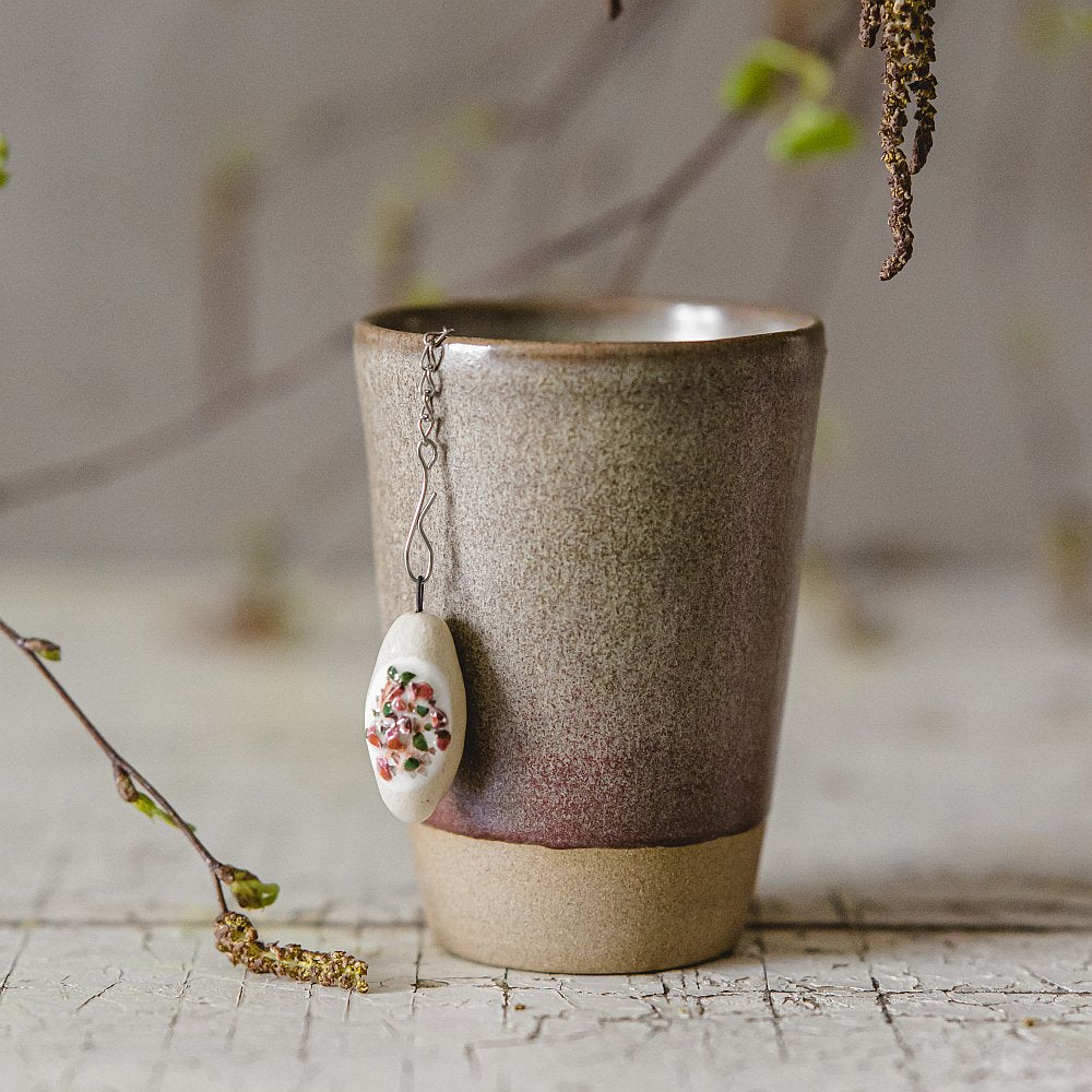 Stainless steel loose leaf tea infuser featuring a hand-made ceramic cepelinas (potato meat dumpling) charm hanging from the chain.