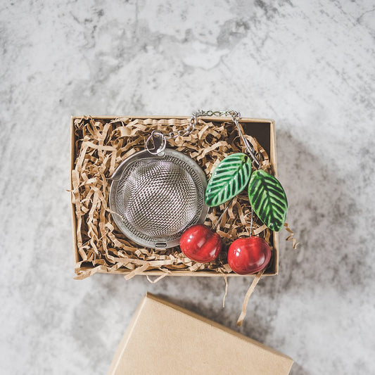 Tea infuser with ceramic cherries with leaves hanging from the chain. Packed in a paper gift box.