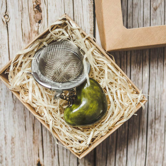 Tea infuser with ceramic green heart hanging from the chain. Packed in a paper gift box.