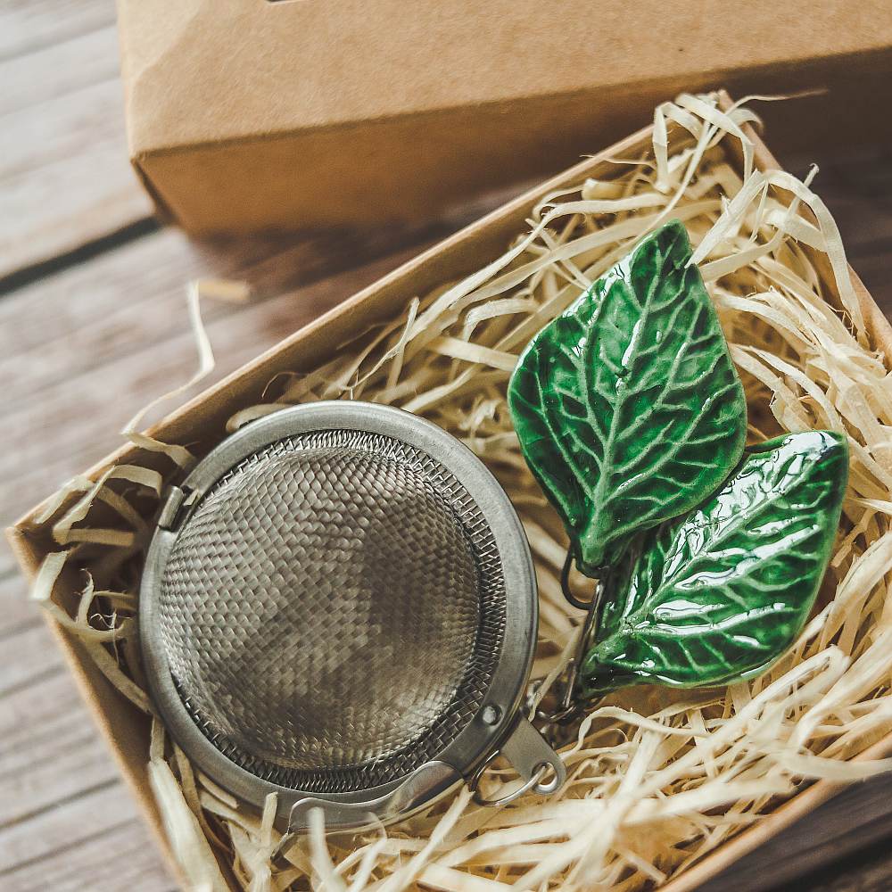 Tea infuser with ceramic green leaves hanging from the chain. Packed in a paper gift box.