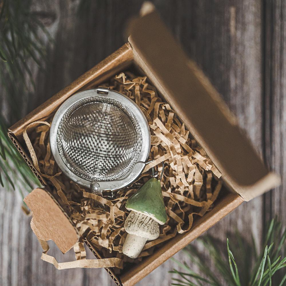 Tea infuser with ceramic green mushroom hanging from the chain. Packed in a paper gift box.