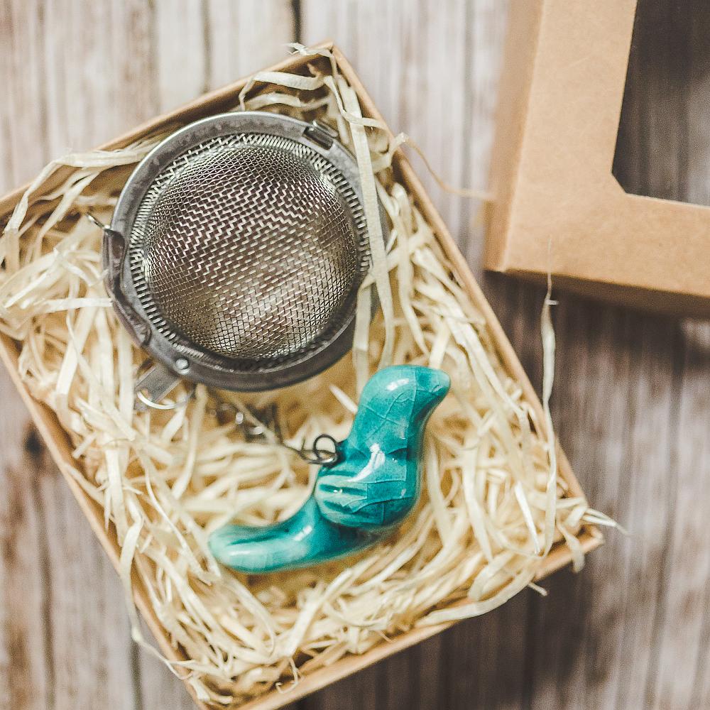 Tea infuser with ceramic light blue bird hanging from the chain. Packed in a paper gift box.