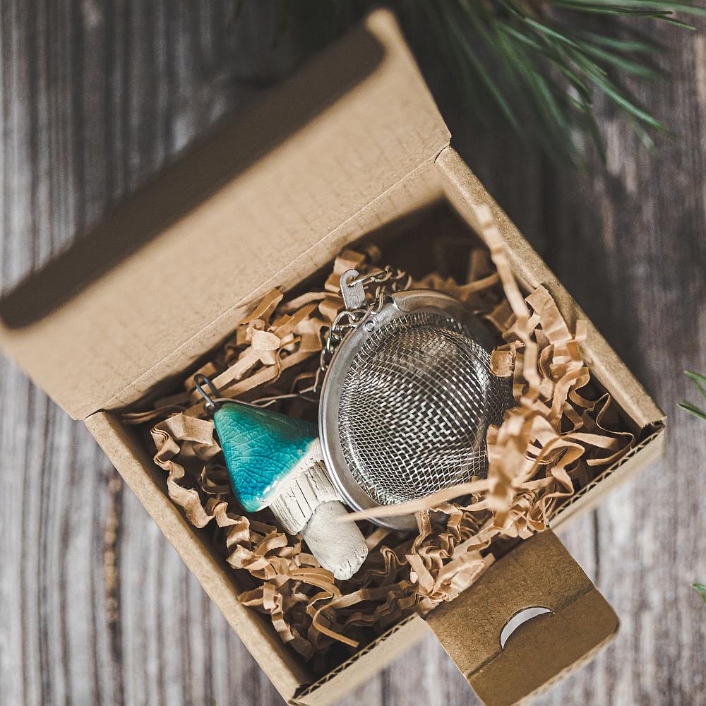 Tea infuser with ceramic light blue mushroom hanging from the chain. Packed in a paper gift box.