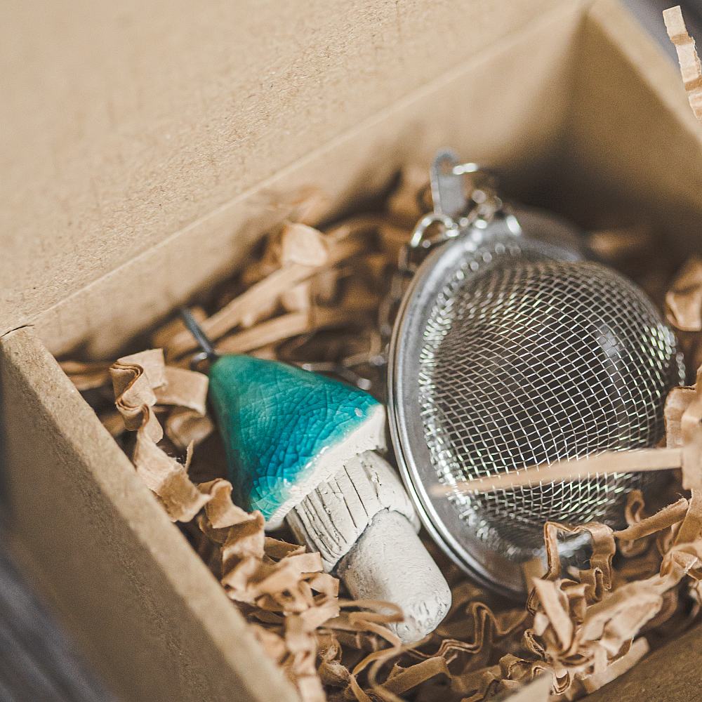 Tea infuser with ceramic light blue mushroom hanging from the chain. Packed in a paper gift box.