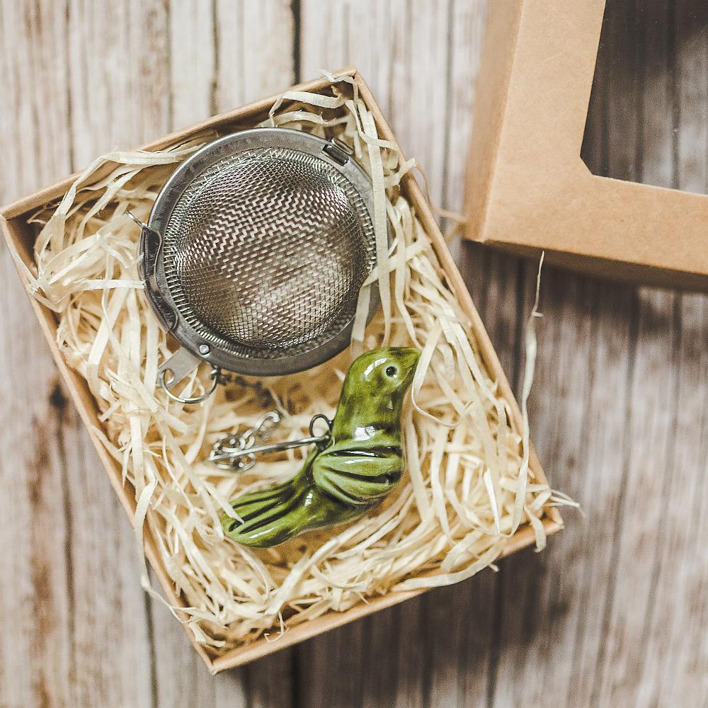 Tea infuser with ceramic moss green bird hanging from the chain. Packed in a paper gift box.
