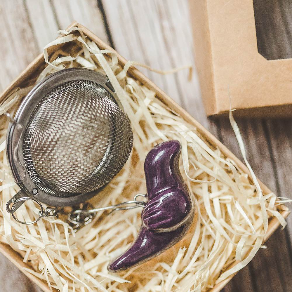 Tea infuser with ceramic purple bird hanging from the chain. Packed in a paper gift box.
