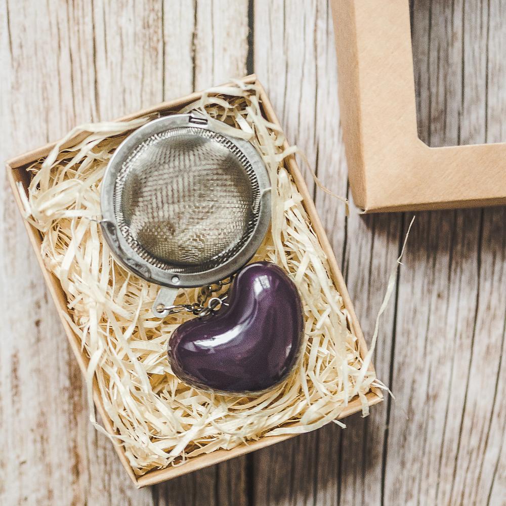 Tea infuser with ceramic purple heart hanging from the chain. Packed in a paper gift box.