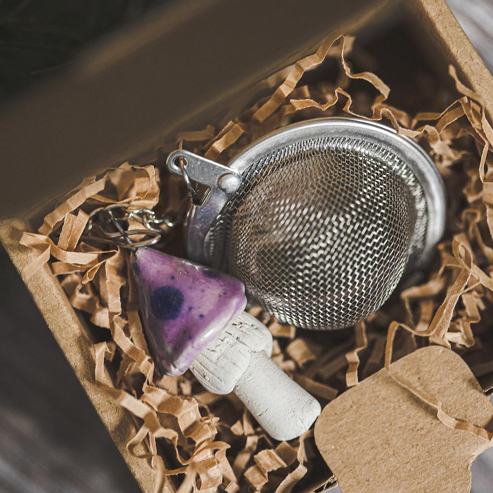 Tea infuser with ceramic purple mushroom hanging from the chain. Packed in a paper gift box.