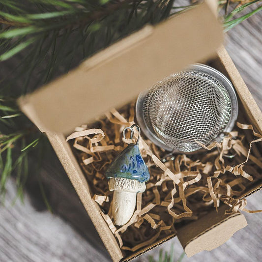 Tea infuser with ceramic swamp blue mushroom hanging from the chain. Packed in a paper gift box.