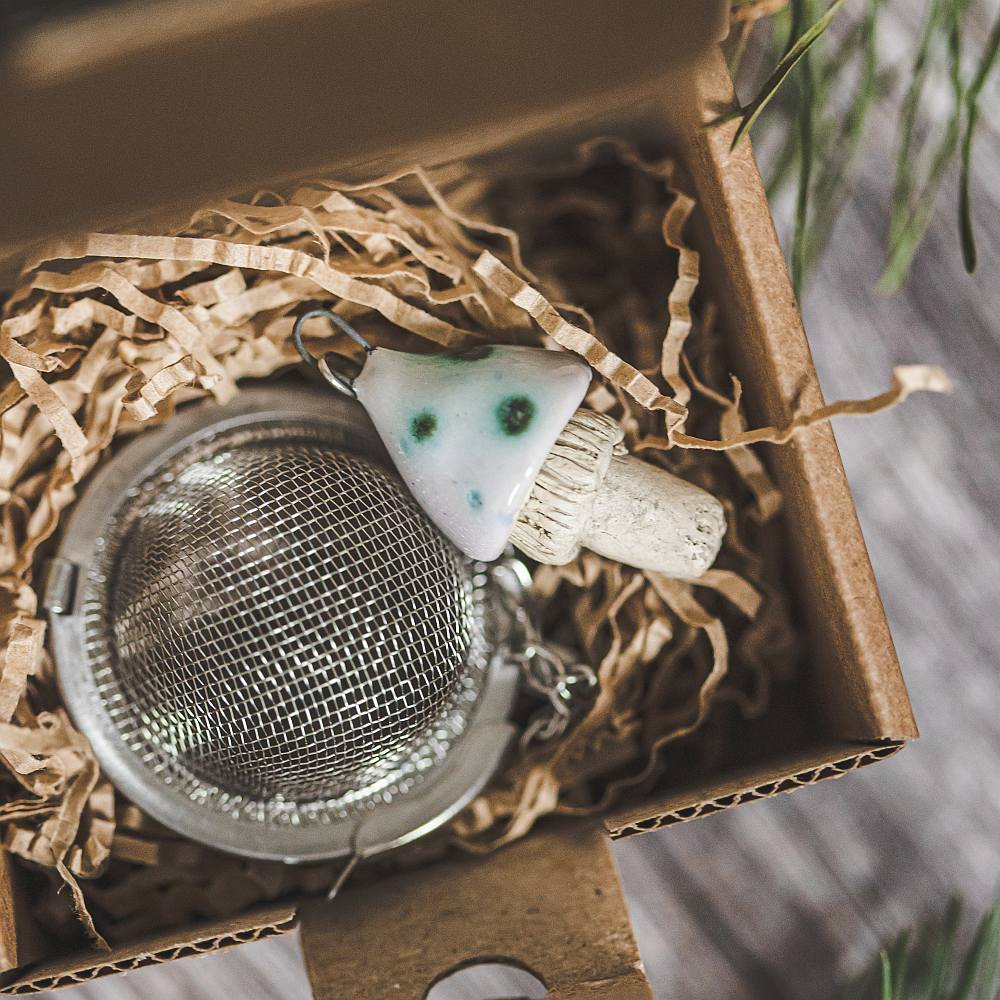 Tea infuser with ceramic swamp mushroom hanging from the chain. Packed in a paper gift box.