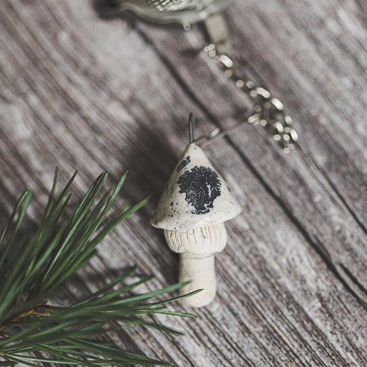 Tea infuser with ceramic white dotted mushroom hanging from the chain.