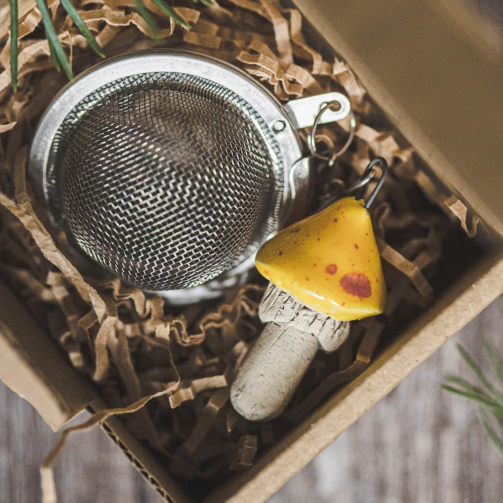 Tea infuser with ceramic yellow dotted mushroom hanging from the chain. Packed in a paper gift box.