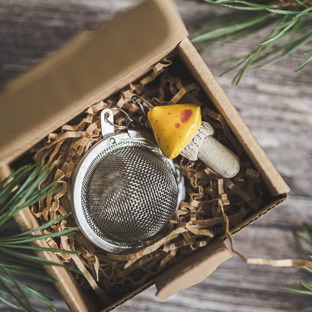 Tea infuser with ceramic yellow dotted mushroom hanging from the chain. Packed in a paper gift box.