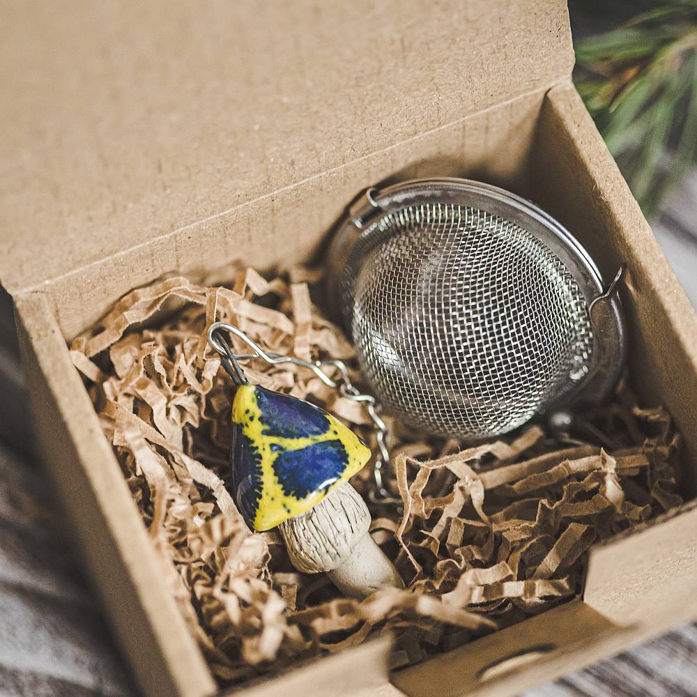 Tea infuser with ceramic yellow spotted mushroom hanging from the chain. Packed in a paper gift box.