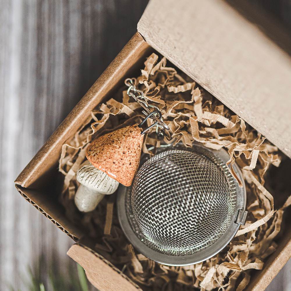 Tea infuser with ceramic yellowish mushroom hanging from the chain. Packed in a paper gift box.