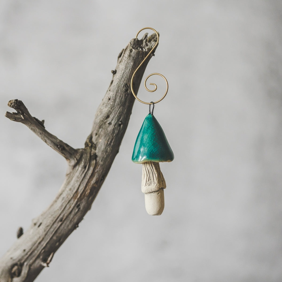 Ceramic turquoise magic mushroom ornament hanging on a branch of Christmas tree.