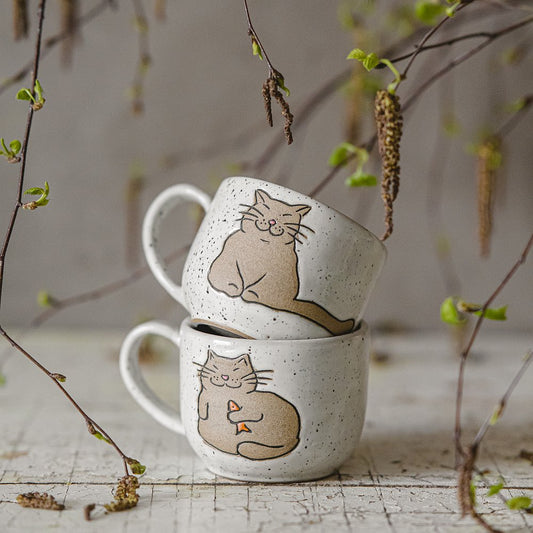 Handmade white ceramic mug with a glossy glaze, featuring an unglazed cat design on the side.