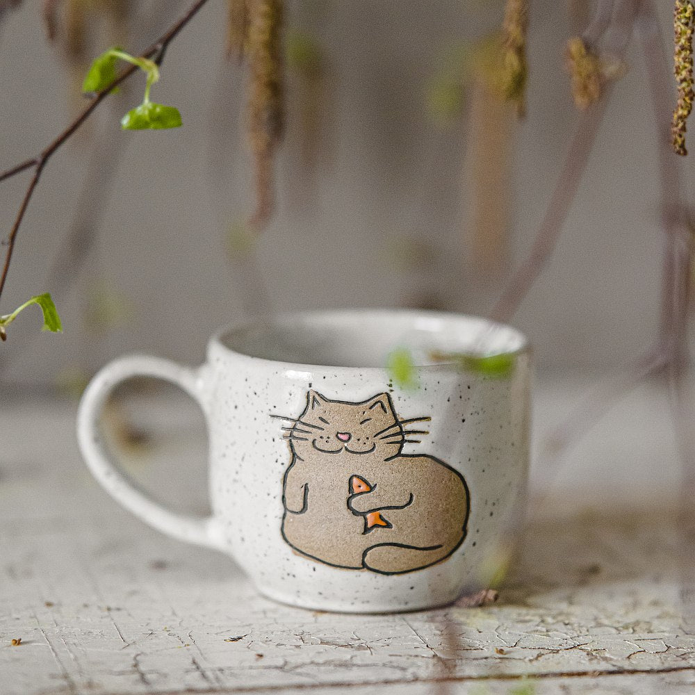Handmade white ceramic mug with a glossy glaze, featuring an unglazed cat design on the side.