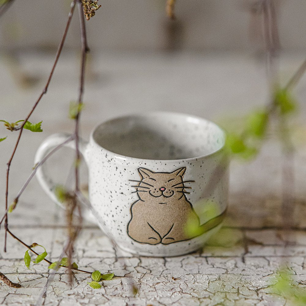 Handmade white ceramic mug with a glossy glaze, featuring an unglazed cat design on the side.