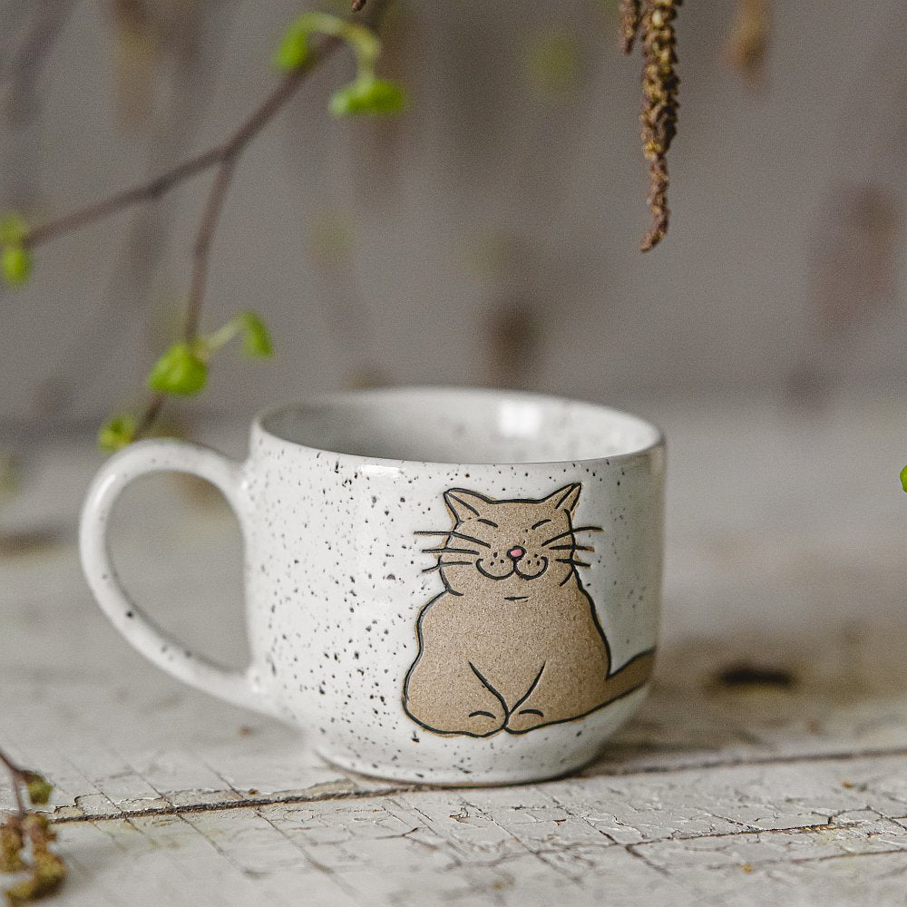 Handmade white ceramic mug with a glossy glaze, featuring an unglazed cat design on the side.