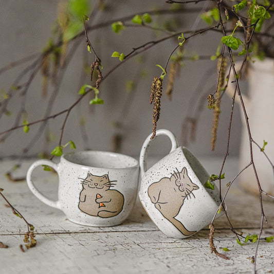 Handmade white ceramic mug with a glossy glaze, featuring an unglazed cat design on the side.
