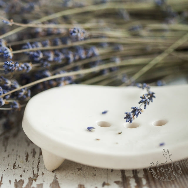 Handmade ceramic oval soap dish. Crafted from white clay and finished with a glossy white glaze. Designed with drainage holes, a concave shape, and four little feet.
