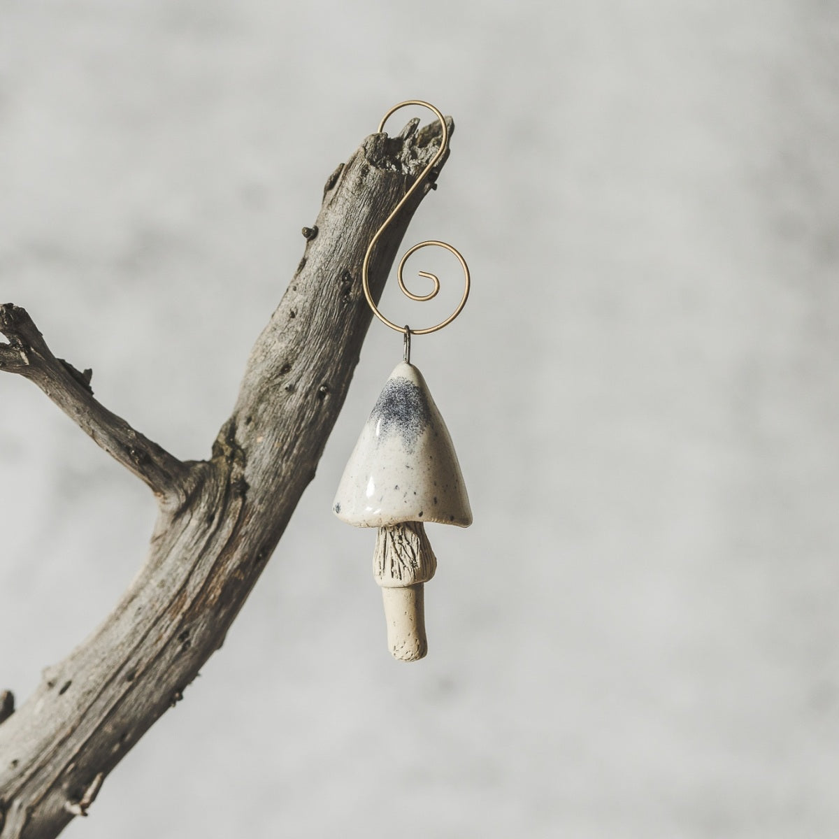 Ceramic white swamp mushroom ornament hanging on a branch of Christmas tree.