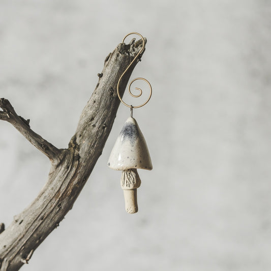 Ceramic white swamp mushroom ornament hanging on a branch of Christmas tree.